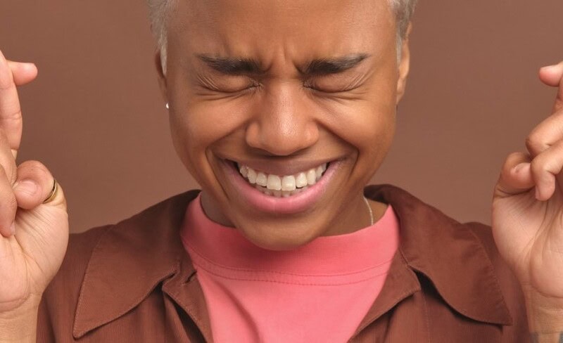 Woman with grimace on face and holding up hands with fingers crossed