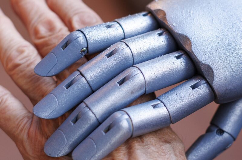 Older adult hand with robotic hand over it.