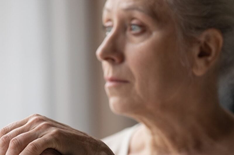Depressed older woman looking sadly out a window