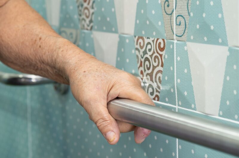 Older person's hand gripping bathroom handrail for safety